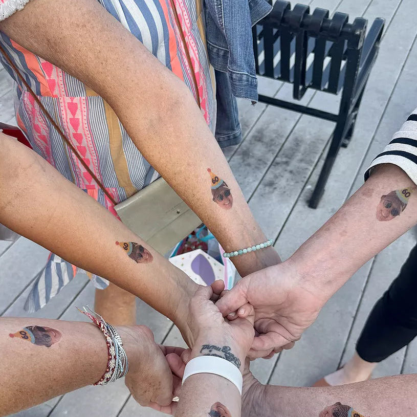 Group of people with matching tattoos on their arms, standing close together on a wooden deck.