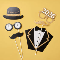 Set of photo booth props including a top hat, mustache, tuxedo, and '2026' on a yellow background