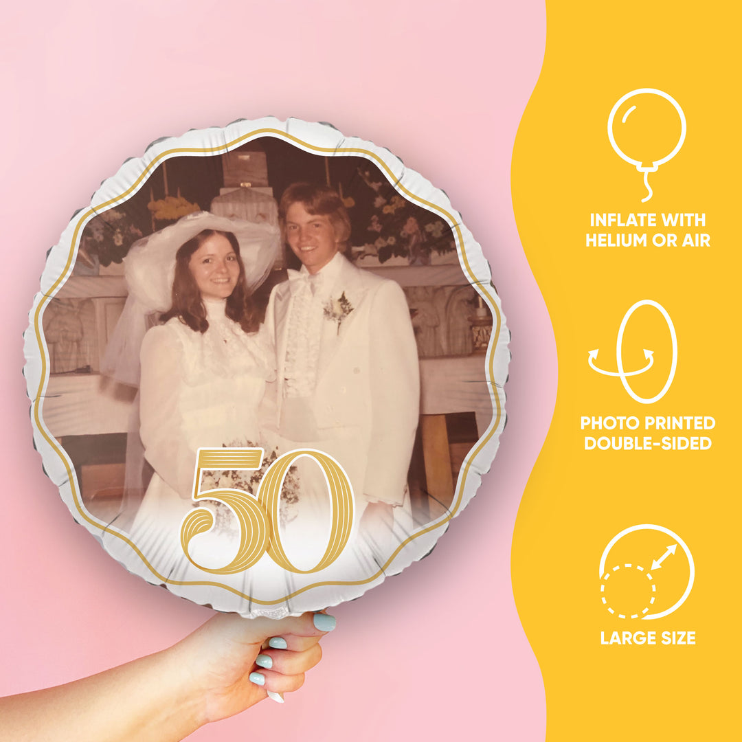 Round balloon with a custom printed photo for 50th wedding anniversary of two people in wedding attire and the number 50, held by a hand against a pink background.