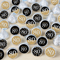 A collection of round candy stickers with gold and black designs, and the number 80 prominently displayed, indicating a celebration for an 80th birthday.
