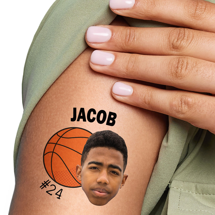 A close-up image of a person's arm with a basketball temporary tattoo that features a basketball, a name 'JACOB', and a jersey number '#24'.