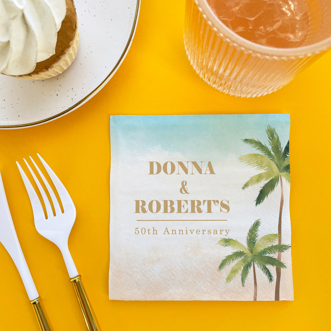 50th Anniversary card with palm trees on a yellow table with cutlery and dessert.