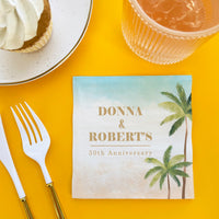 50th Anniversary card with palm trees on a yellow table with cutlery and dessert.