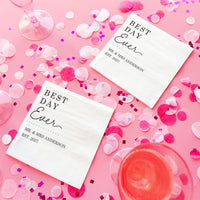 Two 'Best Day Ever' napkins on a pink background with confetti and glasses.