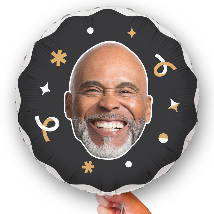 A personalized black and gold balloon with a photo of a smiling person printed on it, decorated with stars and confetti.