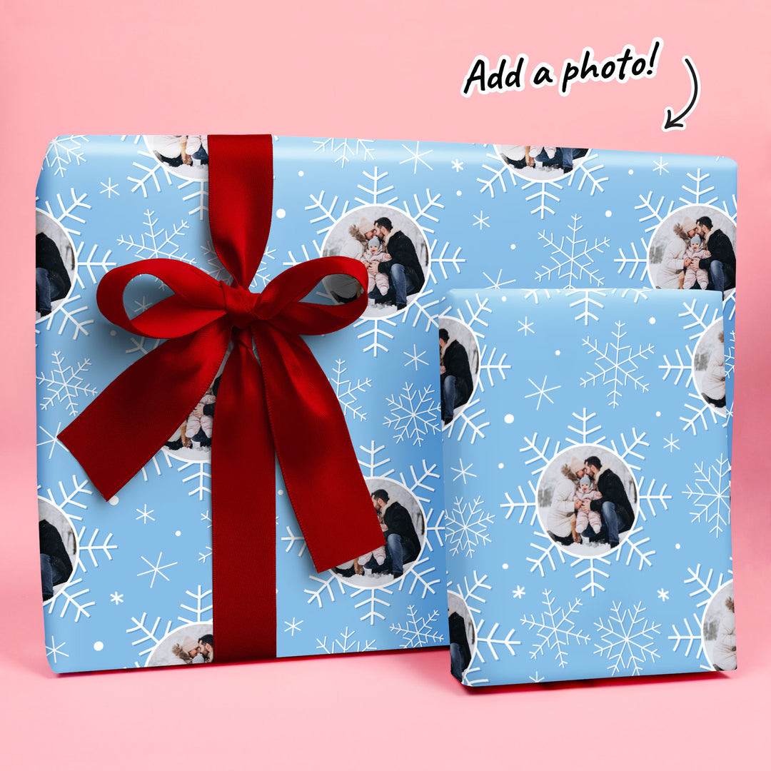 Blue gift wrap with snowflakes and a red ribbon on a pink background