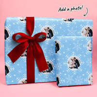 Blue gift wrap with snowflakes and a red ribbon on a pink background