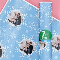 Blue wrapping paper with white snowflakes and a roll of paper on a pink background