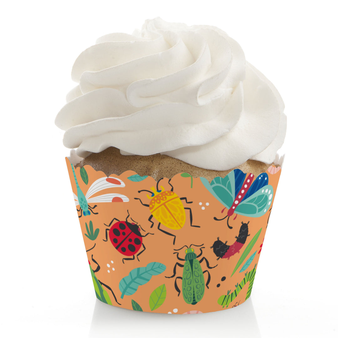 A cupcake with a decorative edge paper wrapper featuring colorful bug illustrations, with a frosted topping.