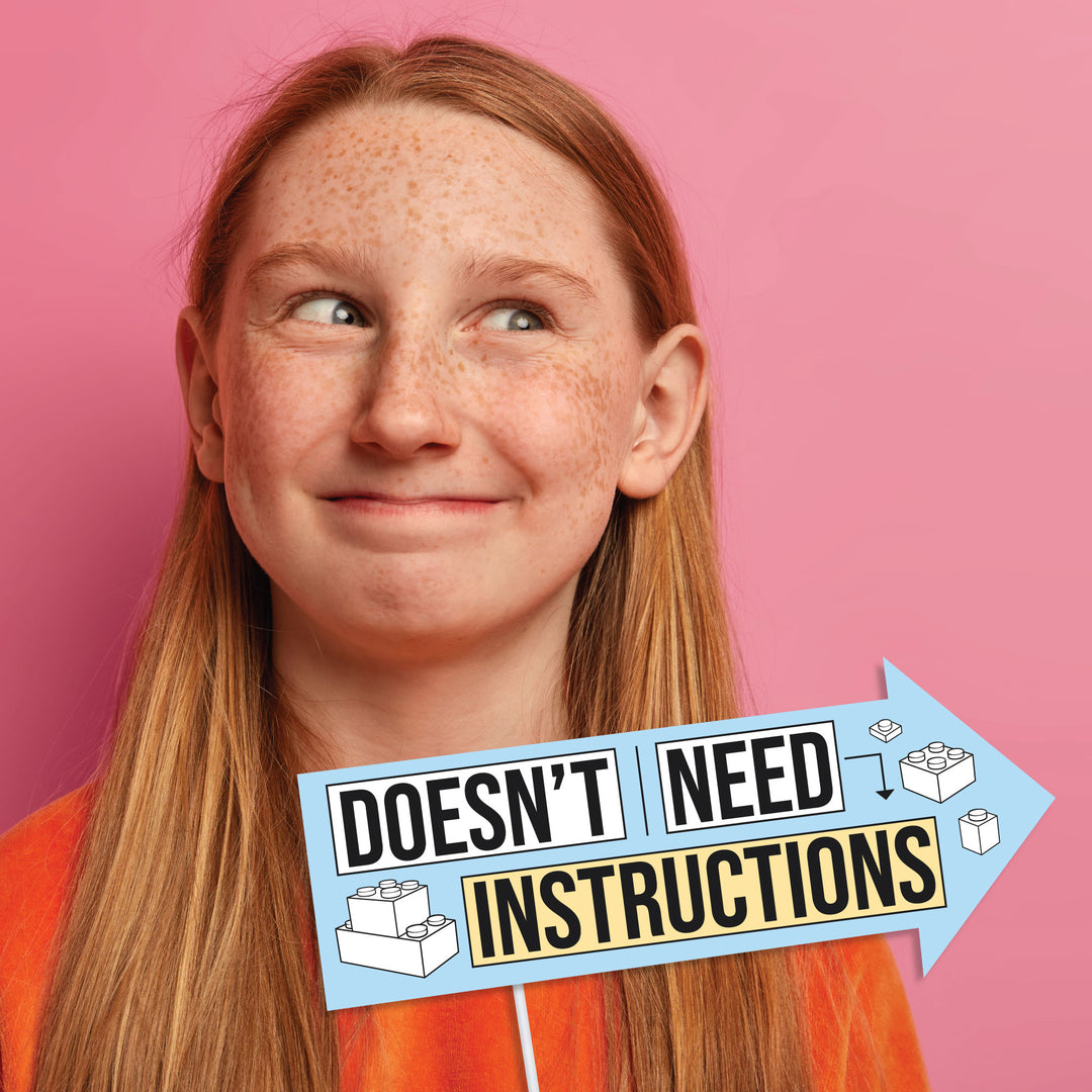 Person with long red hair against a pink background holding a party photo prop with text 'Doesn't Need Instructions'.