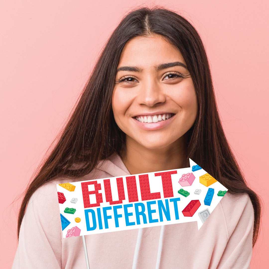 Woman holding a 'Built Different' sign with colorful text and lego blocks on a pink background