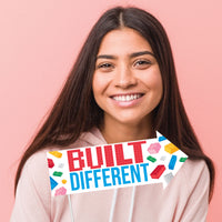 Woman holding a 'Built Different' sign with colorful text and lego blocks on a pink background