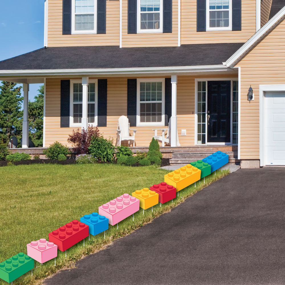Colorful toy building blocks party signs arranged in a line on a lawn in front of a house.