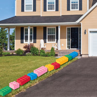 Colorful toy building blocks party signs arranged in a line on a lawn in front of a house.