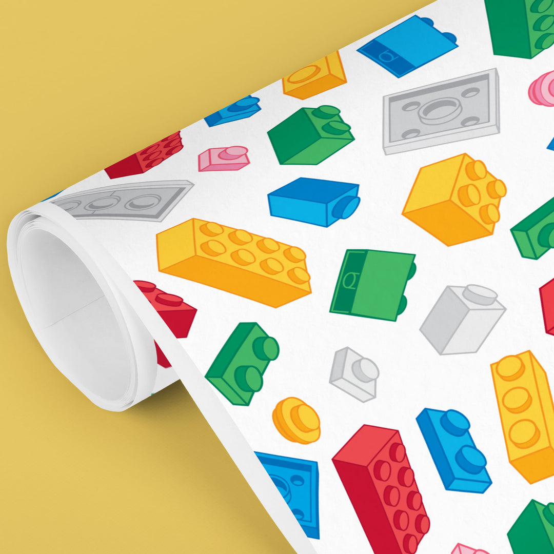 Colorful toy block pattern gift wrapping paper on a white surface with a yellow background