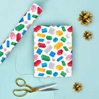 Colorful building block patterned gift wrap paper with scissors and gold bows on a light blue background