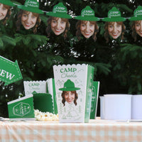 Custom Camp bach themed party supplies with face cutouts and green hats on a table with popcorn.