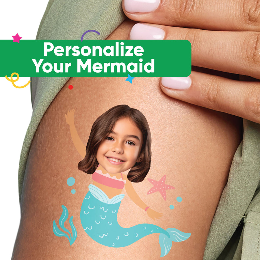 A close-up image of a person's arm with a custom face mermaid temporary tattoo applied to it, featuring a smiling child with mermaid elements like a tail and stars.