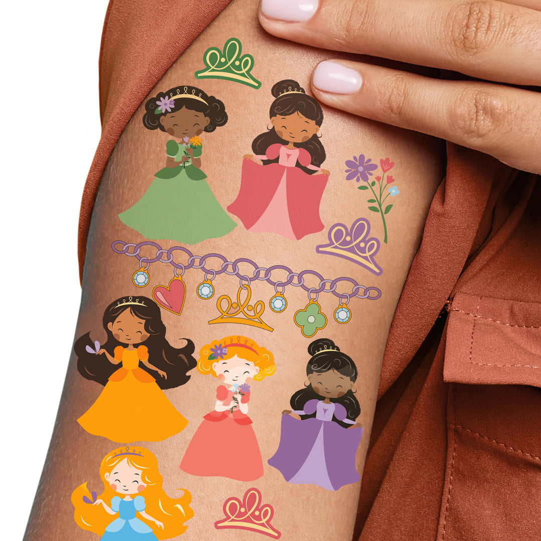 A person's forearm displaying a series of colorful temporary tattoos featuring princesses in various poses and attire, along with elements like crowns and flowers.