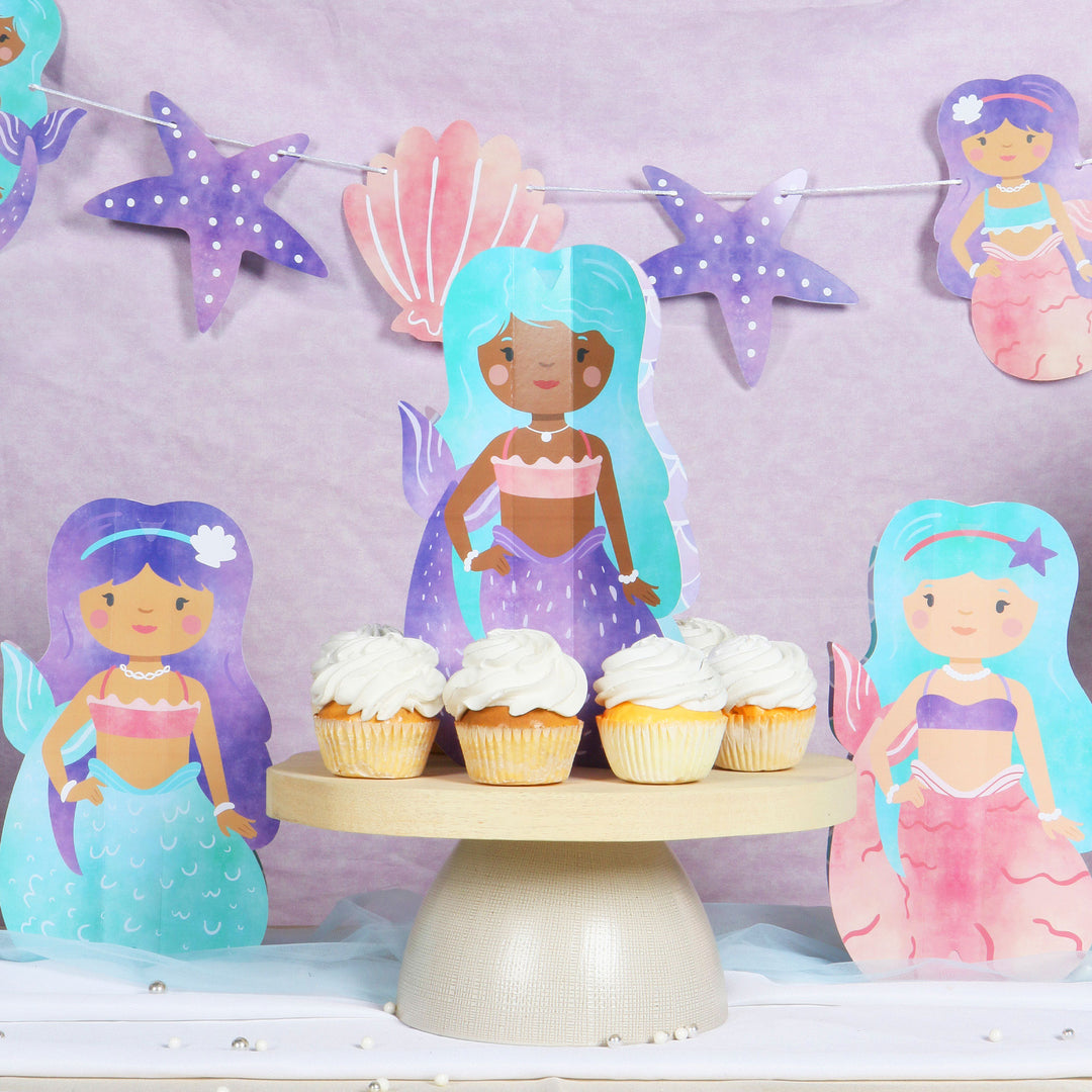 Mermaid shaped centerpieces on a table with a purple background and a seashell party garland banner
