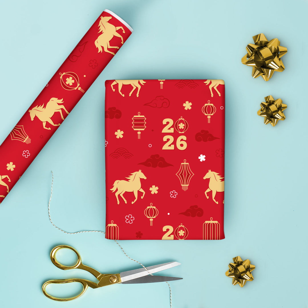 Red gift box with gold horse and lantern patterns, accompanied by red wrapping paper, gold scissors, and decorative bows on a light blue background.
