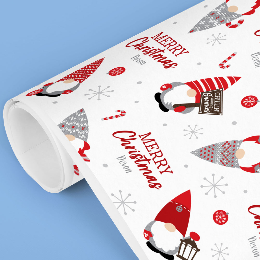 Roll of Christmas-themed wrapping paper with gnomes and 'Merry Christmas' text on a blue background.