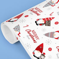 Roll of Christmas-themed wrapping paper with gnomes and 'Merry Christmas' text on a blue background.