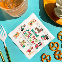 Napkin with Christmas-themed pets designs on a turquoise surface with food items.