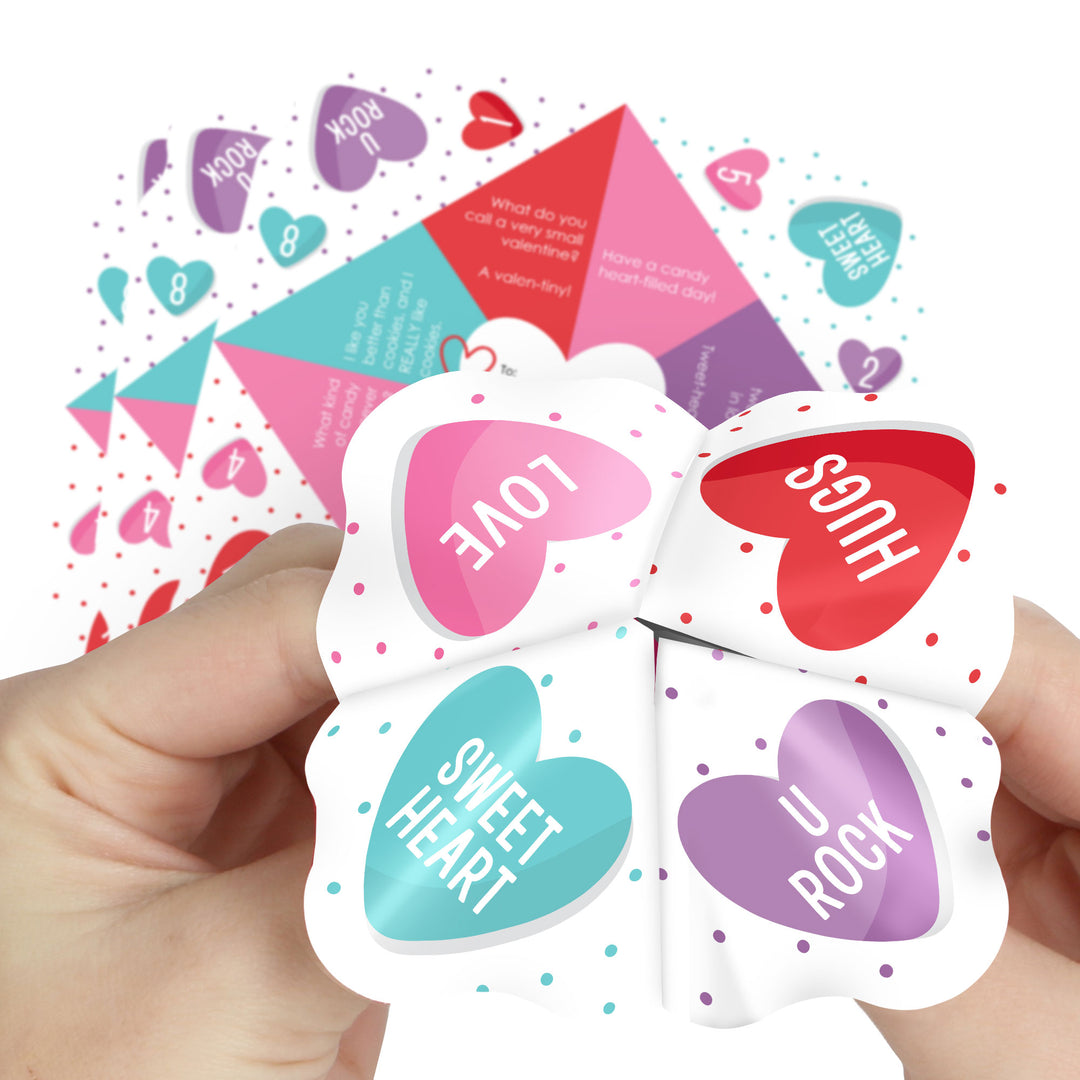 A hand holding several colorful paper fortune tellers with heart shapes and text messages like 'I LOVE YOU', 'SWEET HEART', and 'U ROCK' written on them.