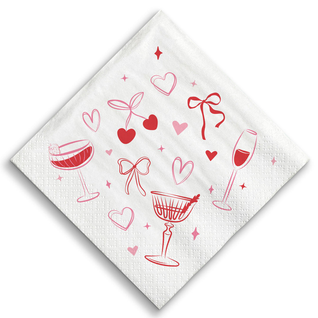 White napkin with red wine glass, heart, and bow designs on a white background