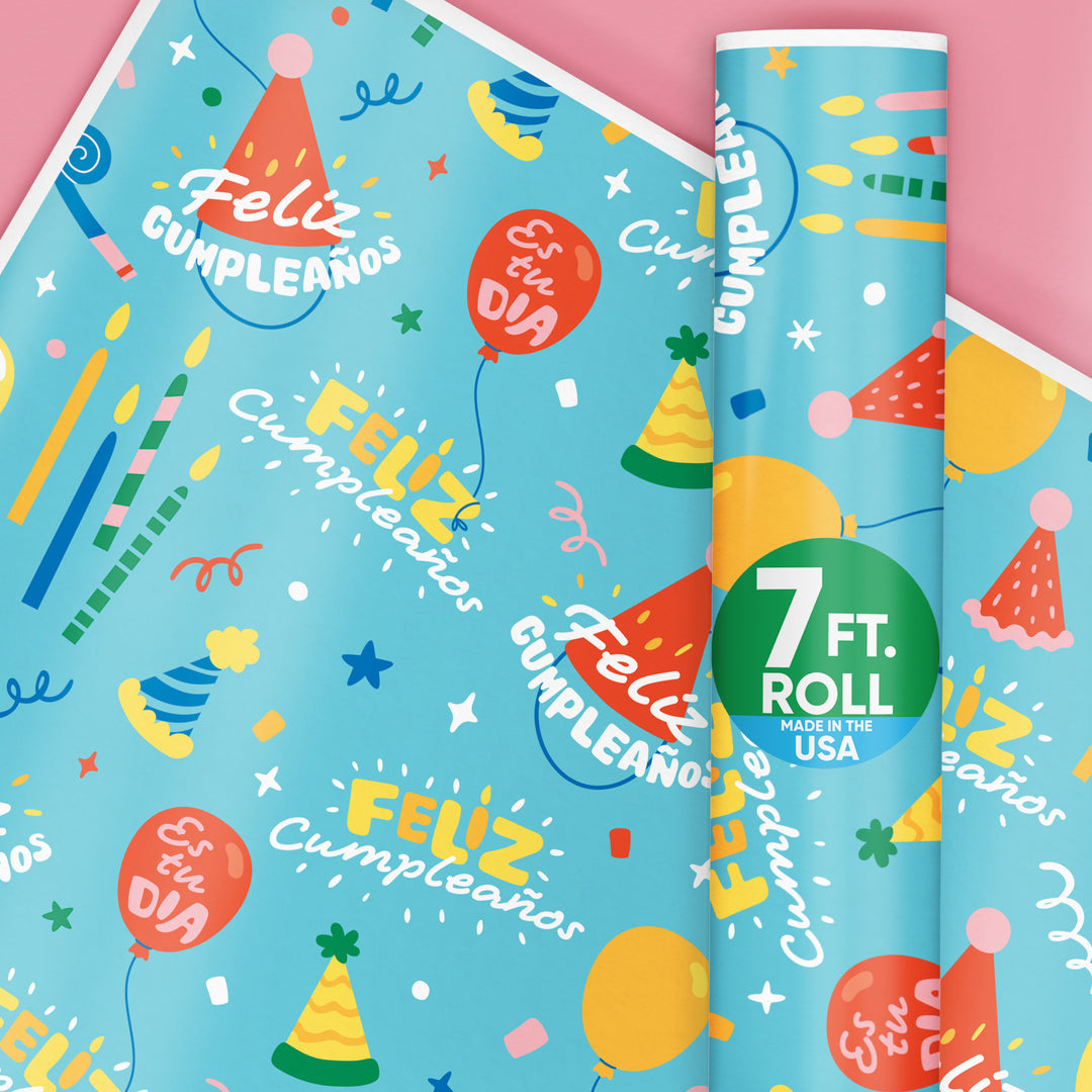 A roll of Feliz Cumpleanos wrapping paper with a fun blue birthday party design, featuring balloons and party hats, wrapped around a pink background.