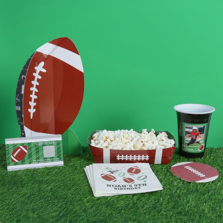 Football-themed party supplies including plates, cups, and napkins on a green surface.