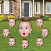 A set of custom yard signs featuring various sized faces arranged in a pattern on a lawn, with a large face in the center and smaller faces around it.