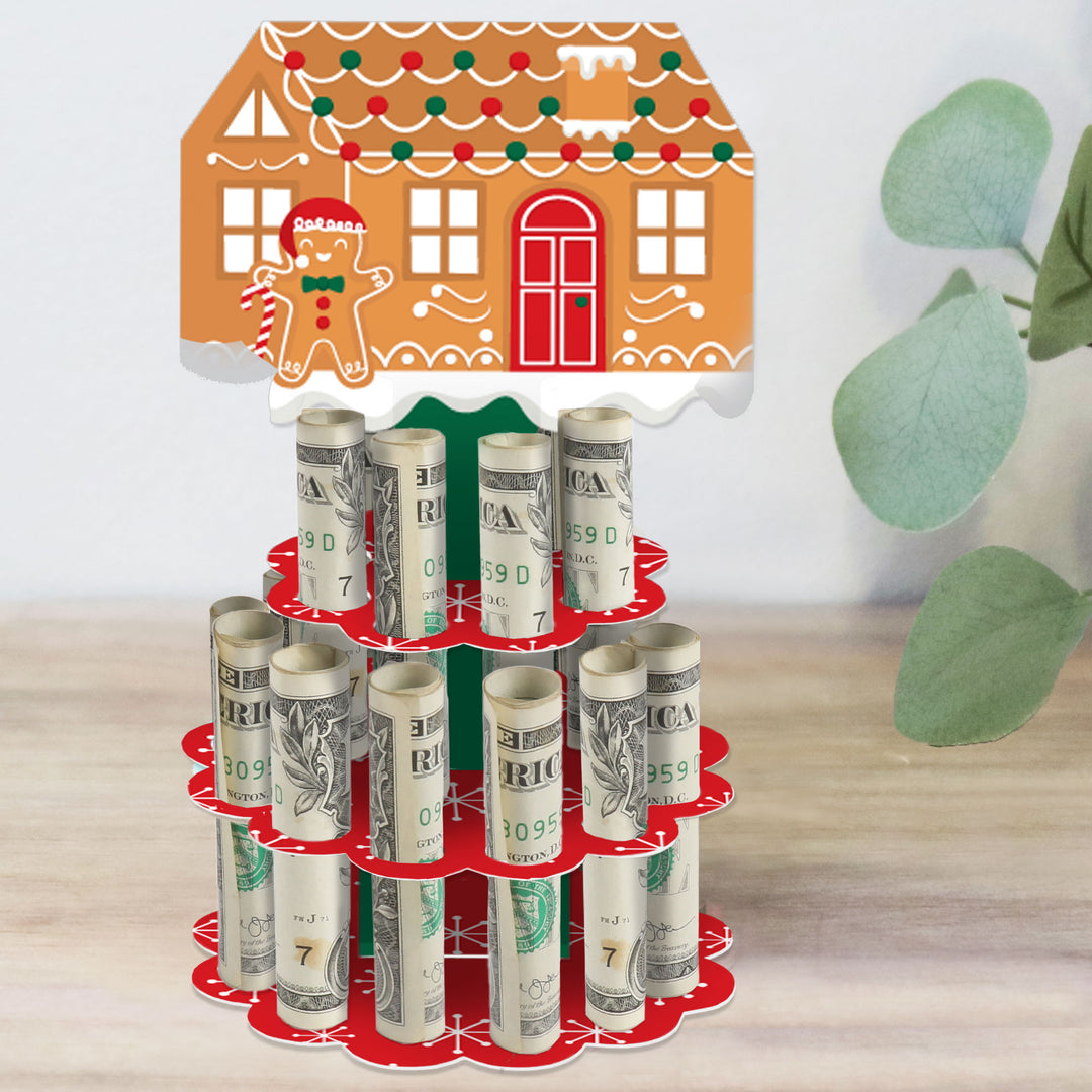 A DIY gingerbread house cash holder gift in a red and green 2-tier cake shape with slots holding rolled-up bills, designed for a Christmas or holiday party.
