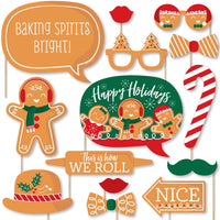 A collection of printed and cut-out photo booth props featuring gingerbread man themes, including signs with holiday greetings, a candy cane, and various facial features like mustaches and lips on sticks.