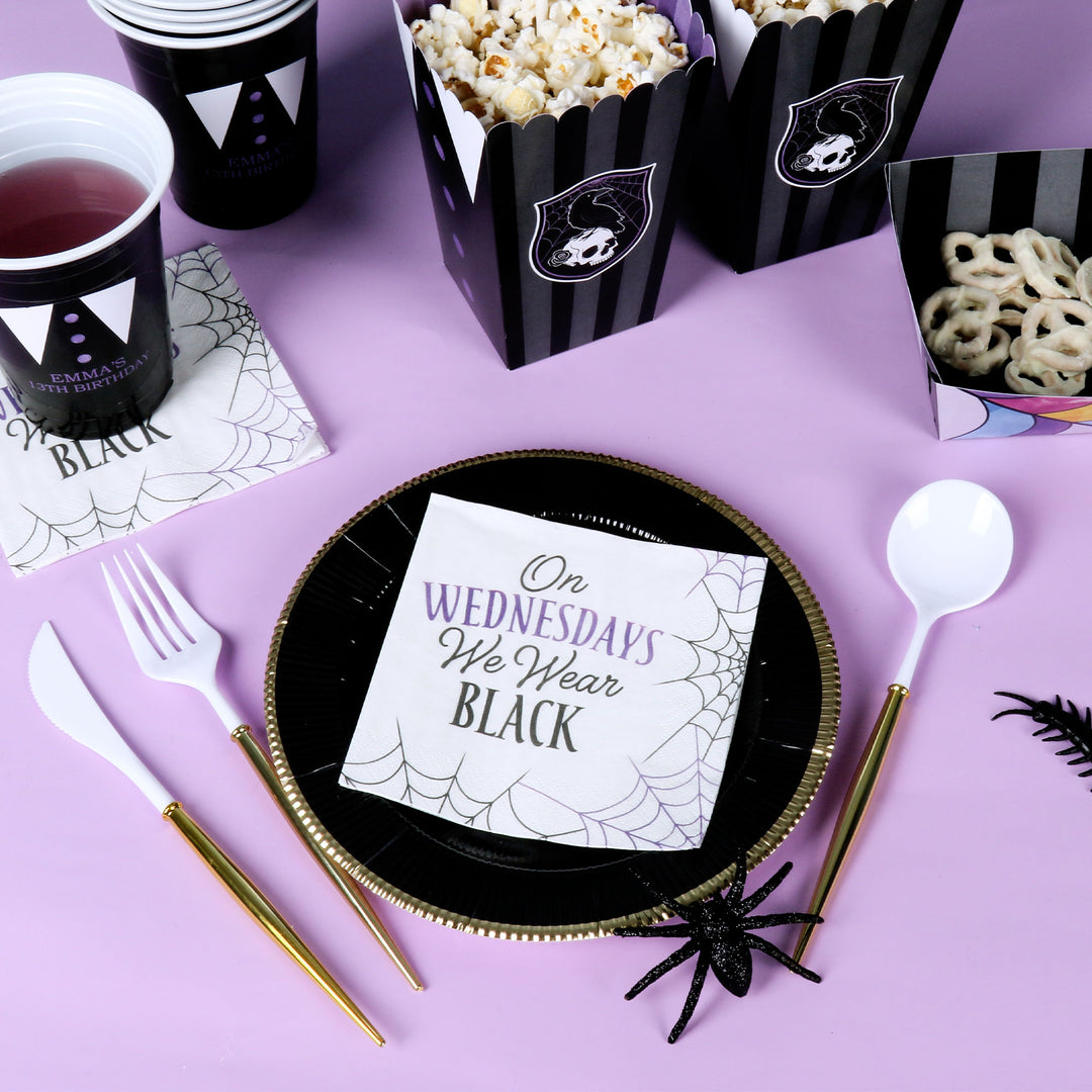 Halloween-themed table setting with black and purple plates, cups, and popcorn boxes on a purple background.