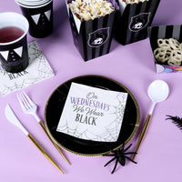 Halloween-themed table setting with black and purple plates, cups, and popcorn boxes on a purple background.