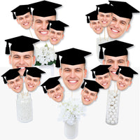 A collection of customized graduation photo head cutouts on sticks, showing various individuals wearing graduation caps. Graduation head on a stick