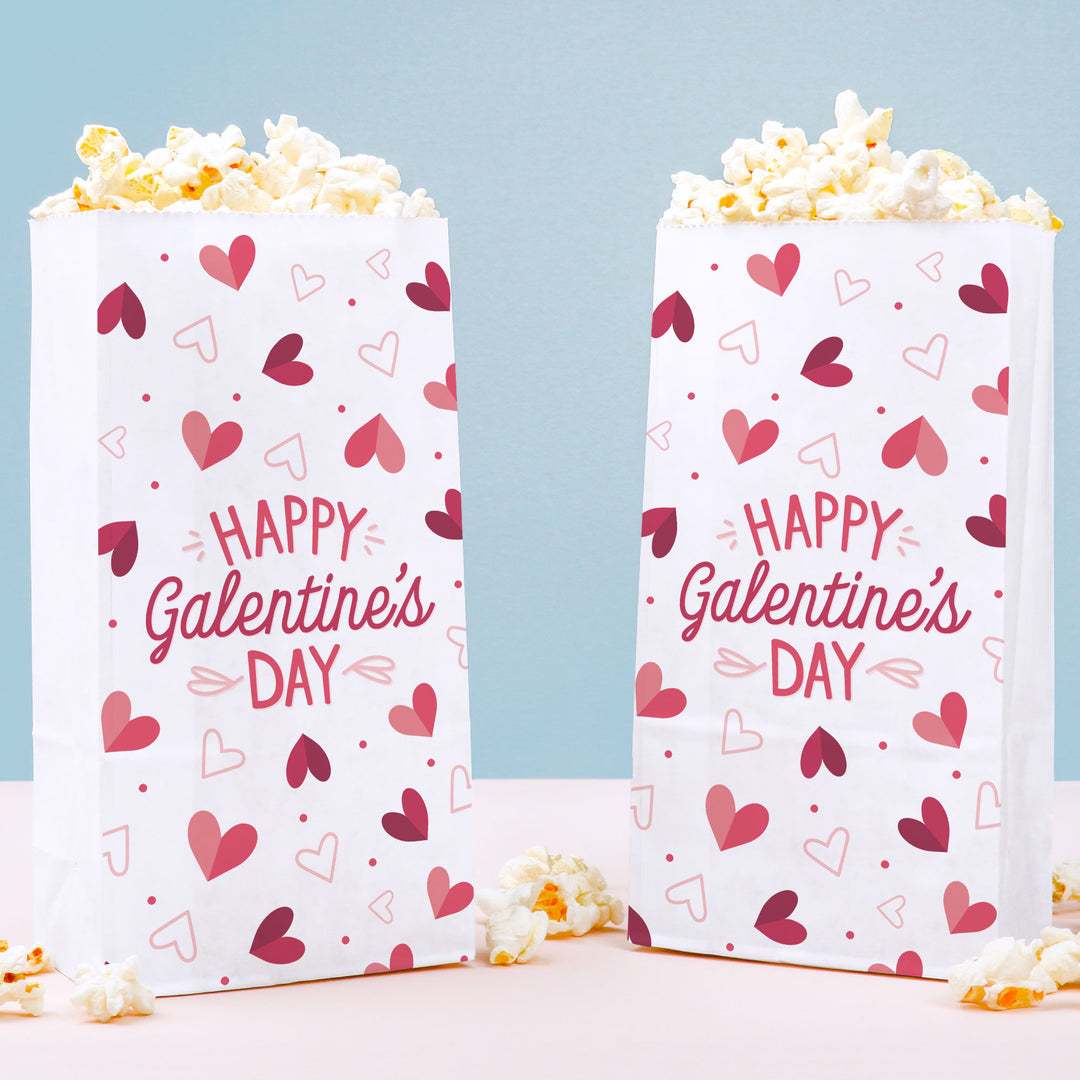 Two popcorn bags with 'Happy Valentine's Day' text and heart patterns on a light blue background.