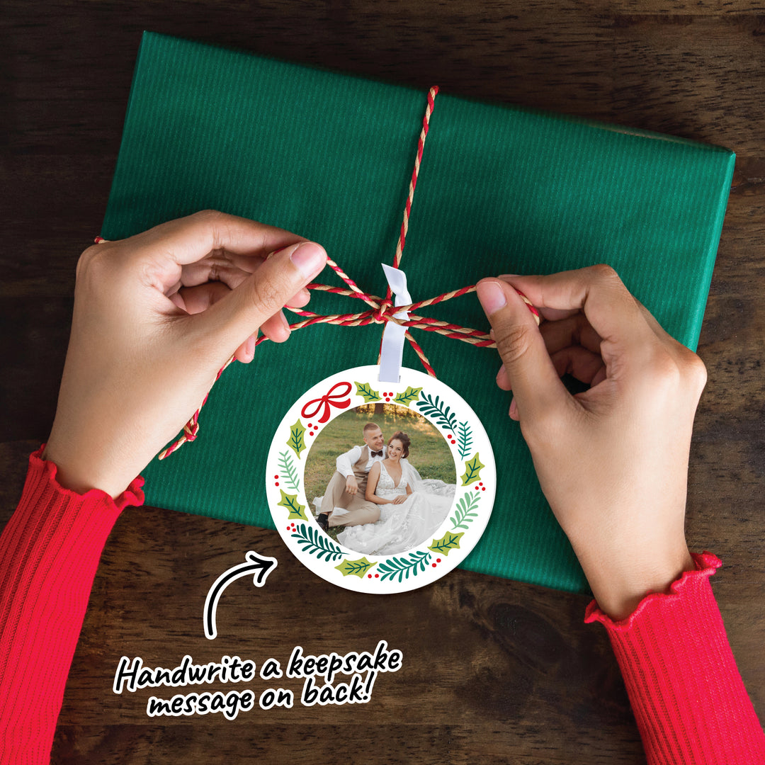 Person attaching a personalized photo ornament to green paper with text 'Handwrite a keepsake message on back!'.