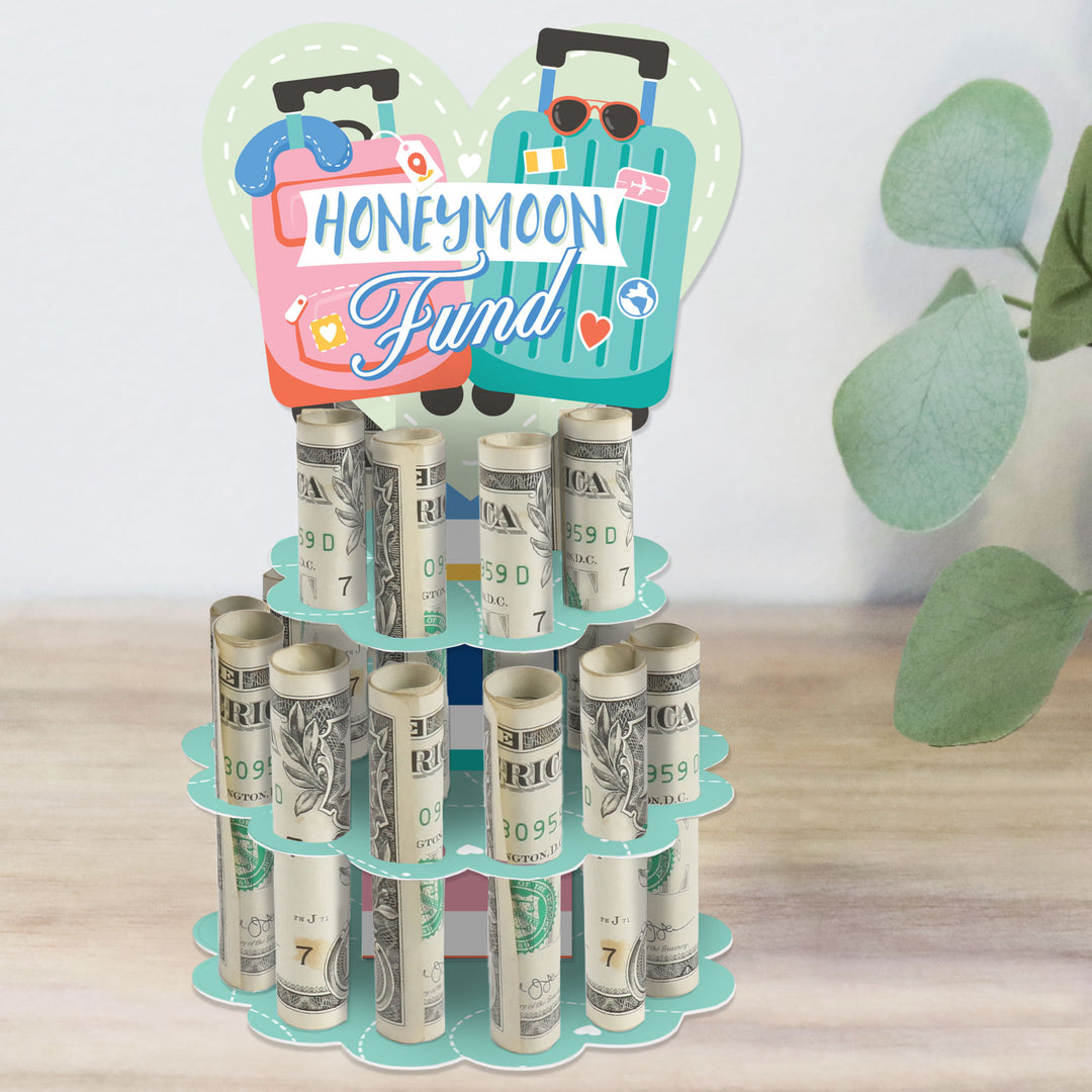 A colorful DIY wedding or engagement party money holder gift designed as a 2-tier cake with 'Honeymoon Fund' text, made from cardboard and holding rolled-up bills in slots.