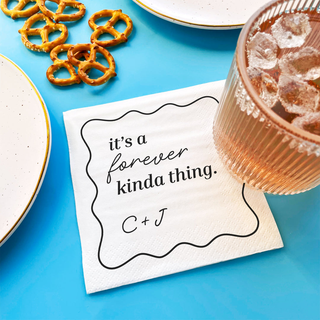 Napkin with 'it's a forever kinda thing' text on a blue surface with pretzels and a drink.