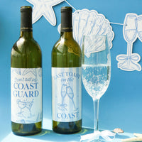 Two wine bottles with humorous labels next to a glass of champagne on a blue background with decorative elements.