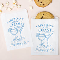 Two 'Last Toast on the Coast Recovery Kit' bags with cocktail graphics and cookies on a light background.