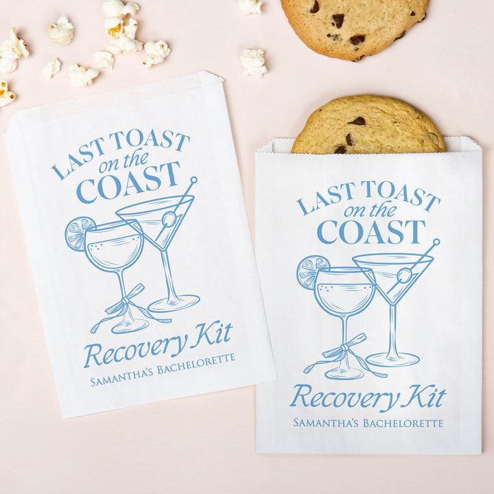 Two 'Last Toast on the Coast Recovery Kit' packages with cookies and popcorn on a light pink background.