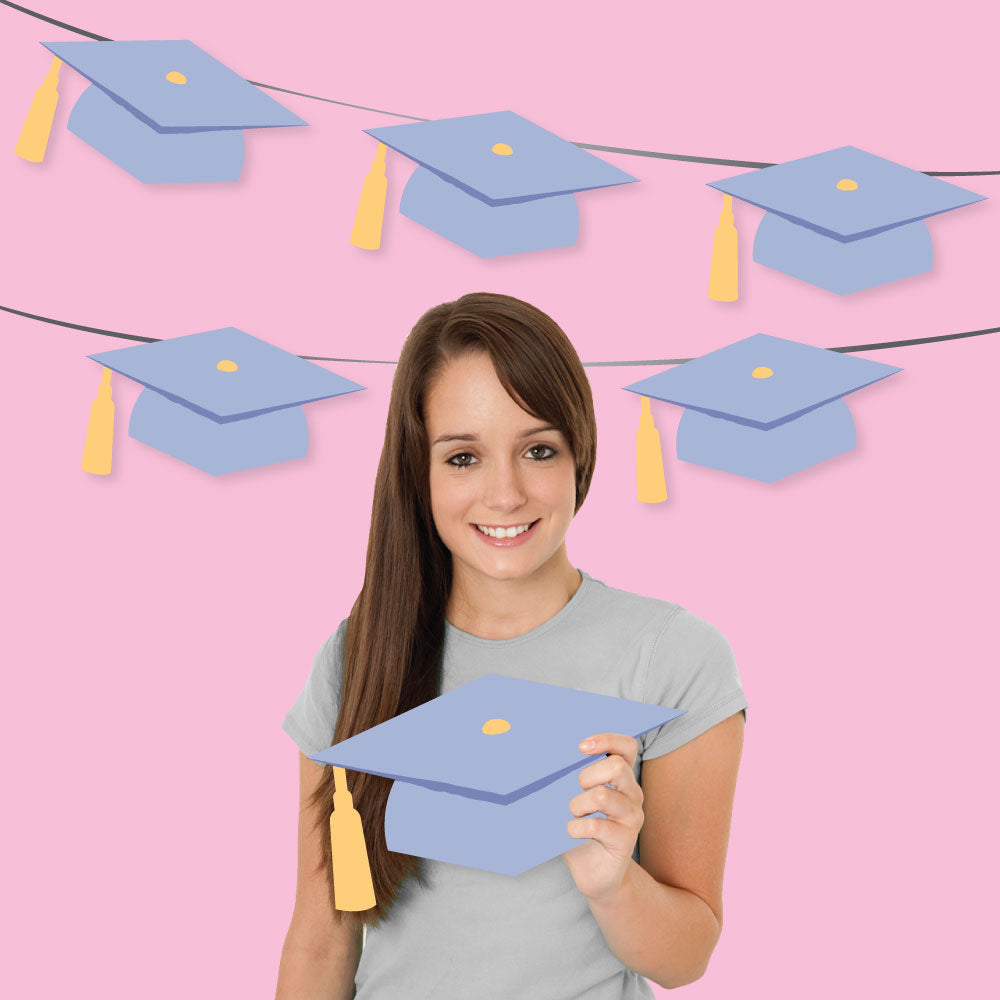Young woman holding a lavender graduation cap against a pink background with paper graduation caps.