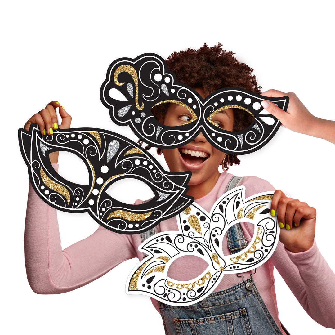 A person holding up three large, decorative masks in black, white, and black with gold accents, designed for use as photo props.