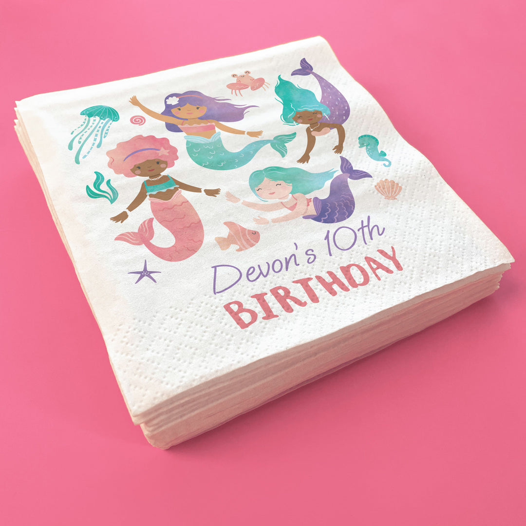Stack of custom birthday-themed napkins with mermaid illustrations on a pink background