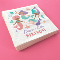 Stack of custom birthday-themed napkins with mermaid illustrations on a pink background