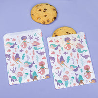 Two mermaid-patterned bags with cookies on a purple background